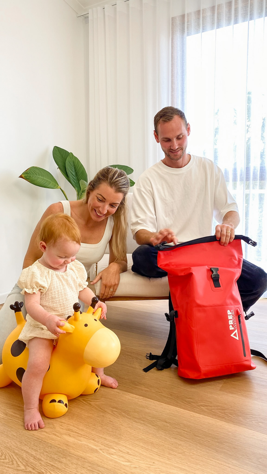 Happy family with a young child in a bright room with a red PrepMates emergency kid waterproof backpack dry bag.